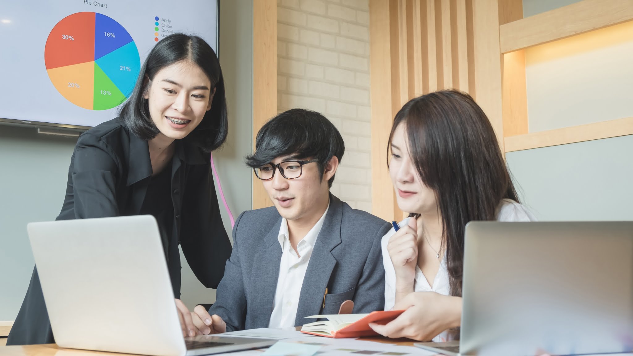 Three Asian business people working on a laptop, focused on a report.