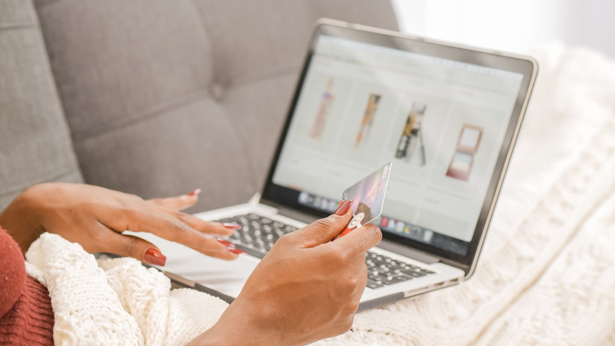 A woman sitting on a couch, using her laptop to search for a product to buy.