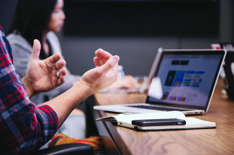 A student explaining, gesturing while sitting at a desk with a laptop.