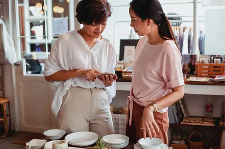 Two women standing in front of a table with dishes, engaged in face-to-face ordering.