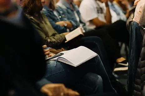 People sitting in a row at a conference, with a student taking notes.